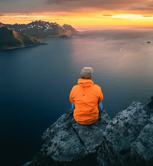 Man sitting on a rock enjoying a beautiful view of water and mountains